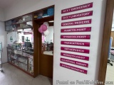 The image shows the entrance of a medical clinic. The entrance has a wooden door and a glass window on the left side. On the...