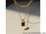 The image shows a gold necklace with a pendant. The pendant is rectangular in shape and has a black stone in the center. The...