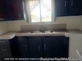 The image shows a kitchen with a sink and a window. The sink has a stainless steel faucet and is located under a white counte...