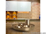 The image shows a set of three stainless steel bowls and a cup on a round tray in a kitchen. The tray is placed on a beige-co...