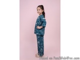 The image shows a young girl standing against a pink background. She is wearing a blue kimono with white floral patterns on i...