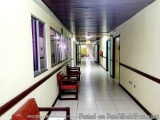 The image shows a long, empty corridor with white walls and a wooden ceiling. The corridor has a tiled floor and there are se...