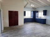 The image shows an empty room with a wooden floor and white walls. The room has a high ceiling with wooden beams and a skylig...