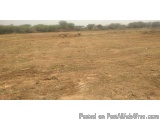 The image shows a vast open field with dry, barren soil. The sky is overcast and the horizon is visible in the distance. The...