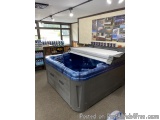 The image shows a large outdoor hot tub in a store. The hot tub is blue and grey in color and has a white cover on top. It ap...