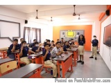 The image shows a classroom with a group of students sitting at their desks. The desks are arranged in rows and the students...