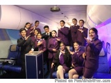 The image shows a group of young people, likely cabin crew members, posing for a photo in an airplane. They are all wearing m...