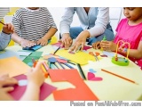 The image shows a group of children sitting around a table with their parents. The table is covered with colorful paper cutou...