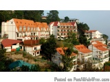 The image shows a group of multi-story buildings with red roofs and white walls. The buildings are arranged in a grid-like pa...