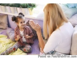 The image shows a young girl sitting on a purple couch with her mother sitting next to her. The girl is wearing a red and whi...