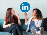 The image shows two young women sitting on a blue couch, engaged in a conversation. They are both smiling and looking at each...