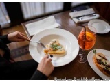 The image shows a person sitting at a table with two plates of food and a glass of orange juice. The person is holding a fork...
