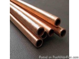 The image shows a group of six copper pipes arranged in a horizontal line on a black surface. The pipes appear to be made of...