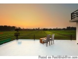 The image shows a beautiful sunset over a vast green field. The sky is painted in a warm orange hue, with the sun partially v...