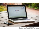 The image shows a laptop computer sitting on a wooden table. The laptop is open and the screen is turned on, displaying the G...