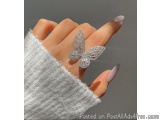 The image shows a close-up of a woman's hand with a ring on it. The ring is in the shape of a butterfly with intricate detail...