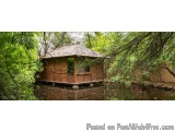 The image shows a small wooden cabin in the middle of a pond. The cabin is made of wood and has a sloping roof with a small w...