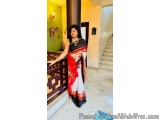 The image shows a young woman standing on a staircase in a traditional Indian outfit. She is wearing a black and red saree wi...