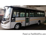 The image shows a white bus parked inside a large warehouse. The bus has a sleek design with a curved roof and large windows...