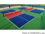 The image shows an outdoor tennis court with multiple blue and red tennis courts. The court is surrounded by a green fence an...