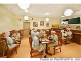 The image shows a group of elderly people sitting at a long wooden table in a restaurant. The table is set with plates, glass...