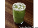 The image shows a tall glass filled with a green drink. The drink appears to be a smoothie or a cocktail, as there are small...