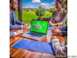 The image shows a group of four people sitting around a wooden table in a meeting room. On the table, there is a laptop with...
