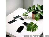 The image shows a white table with several black smartphones scattered on it. On the right side of the table, there is a pott...
