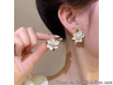 The image shows a close-up of a woman's ear. She is wearing a pair of earrings with a white flower design. The earrings are m...