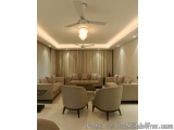 The image shows a modern living room with a high ceiling and a ceiling fan. The room has a beige color scheme and is decorate...