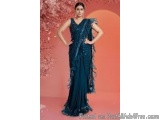 The image shows a woman wearing a long, flowing blue saree. The saree is made of a luxurious fabric with intricate patterns a...