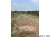 The image shows an empty field with a clear blue sky in the background. The field appears to be dry and barren, with patches...