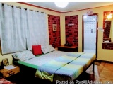 The image shows a bedroom with a single bed in the center. The bed is made up with a green and blue striped comforter and two...