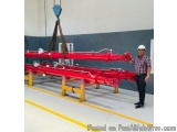 The image shows a man wearing a white hard hat and a plaid shirt standing next to a large red crane. The crane is lifting a l...