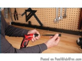 The image shows a person's hand holding a red and black power drill. The person is holding the drill with both hands and appe...