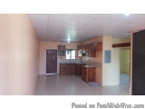 The image shows an empty room with a kitchen and living area. The walls are painted in a light peach color and the floor is m...