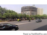 The image shows a busy street in an urban area. The street is lined with trees and there are several cars and motorcycles on...