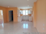 The image shows an empty room with orange walls and white flooring. The room has a large window on the right side, allowing n...