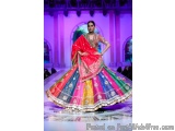 The image shows a model walking on a ramp during a fashion show. The model is wearing a traditional Indian outfit, which is a...