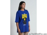 The image shows a young woman wearing a blue t-shirt with a graphic design on the front. The design features a cartoon charac...