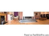 The image shows a modern living room with a large fireplace in the center. The fireplace is made of wood and has a white mant...