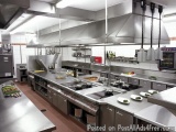 The image shows a modern commercial kitchen with a large stainless steel countertop and a long island in the center. The coun...