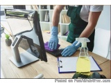 The image shows a person wearing a green apron and blue gloves cleaning a desk with a computer monitor. The person is using a...