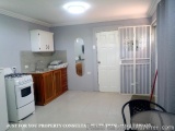 The image shows a small kitchen with a white gas stove and oven on the left side, a sink and a countertop with a mirror above...