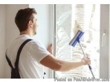 In this image, we can see a man cleaning a window with a squeegee. He is wearing a white t-shirt and black suspenders and is...
