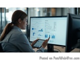 The image shows a young woman sitting at a desk in front of a computer monitor. She is wearing a gray shirt and has long brow...