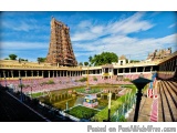 The image is a photograph of a Hindu temple in India. The temple is located in a park-like setting with a clear blue sky in t...
