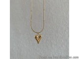 The image is of a gold necklace with a small pendant in the shape of a heart. The necklace is made of a thin gold chain with...