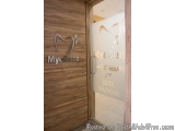 The image shows the entrance of a dental clinic. The door is made of wood and has a glass panel with the logo of MyDent on it...