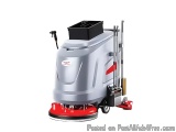The image shows a floor scrubber machine. It is a large, grey machine with a red base and a black bucket on top. The machine...